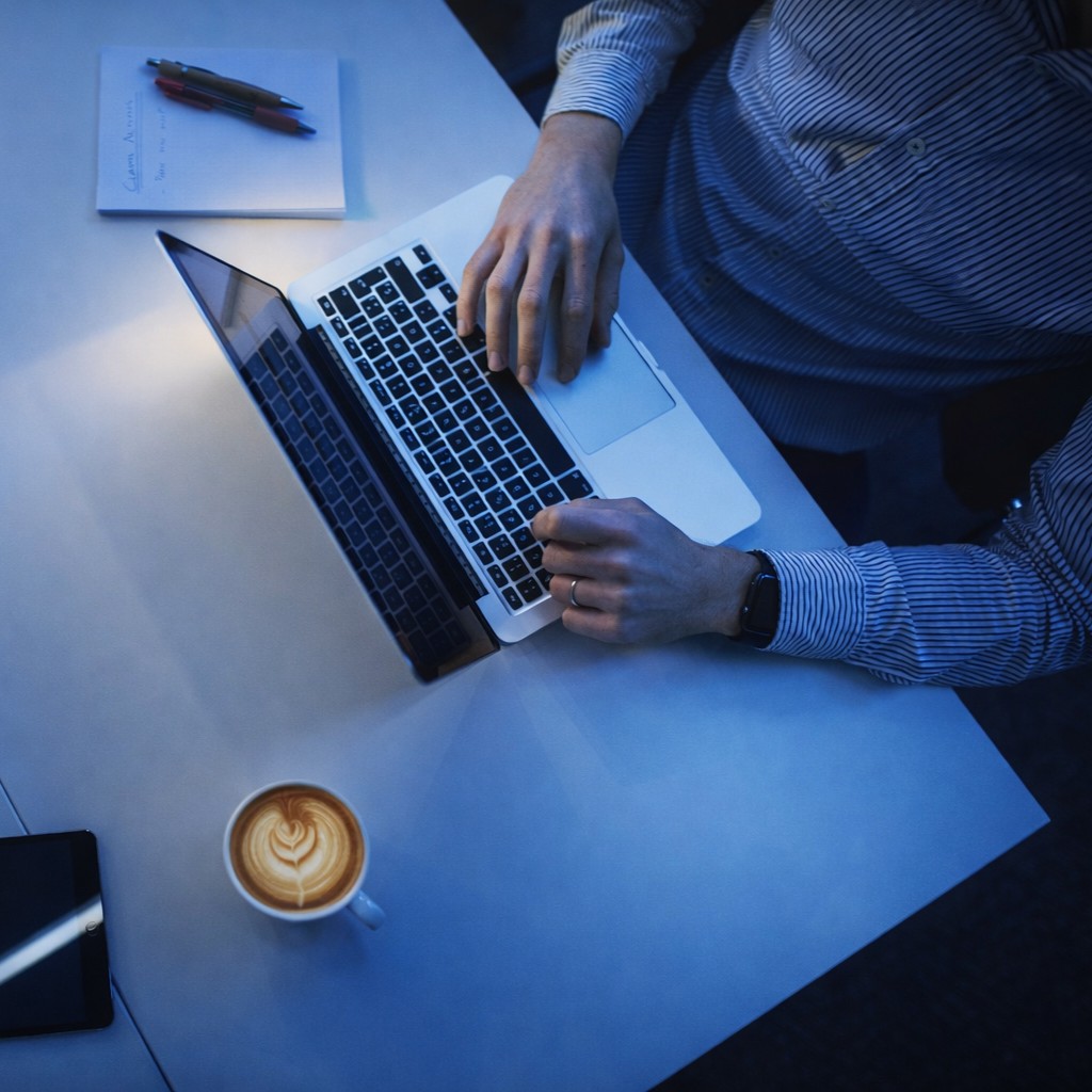 Application development visual - Overhead view of a person using a laptop at a desk with a notebook, smartphone, and latte.