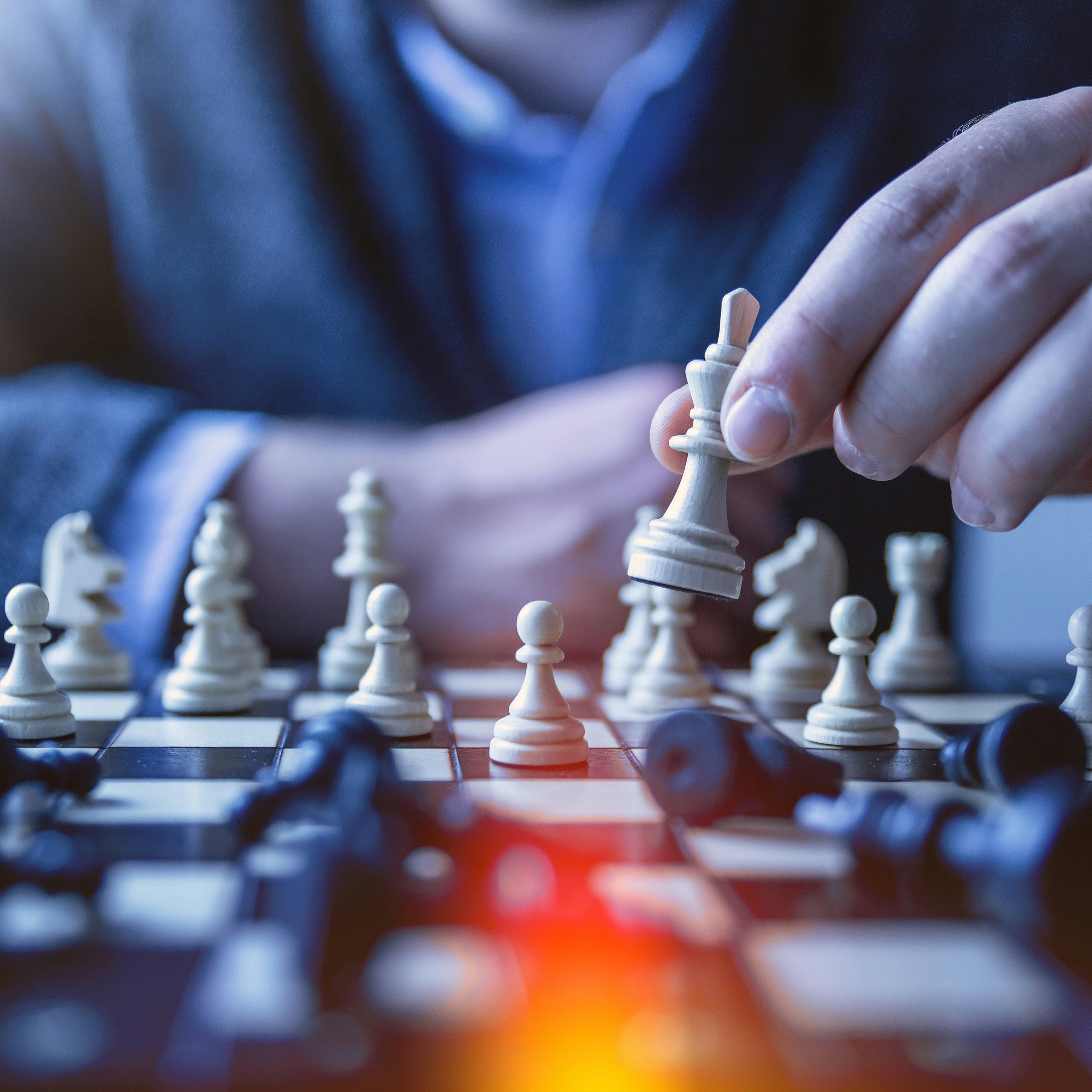Strategic development visual - Close-up of a person moving a white king piece over a chessboard with black pieces in the foreground.