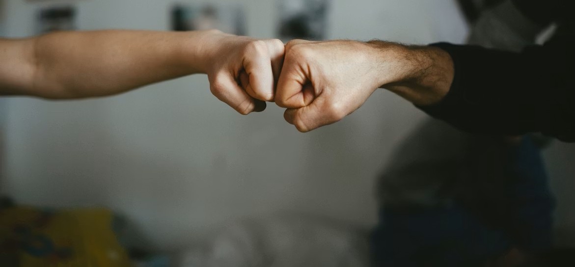 Close-up of two people exchanging a fist bump against a blurred indoor background.